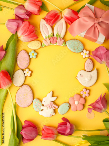 Sweets, pastry, gingerbread cookies for Easter table. Easter eggs, rabbit and tender simple flowers and tulips on yellow background, spring seasonal holiday wreath, banner for your site, flyer, coupon
