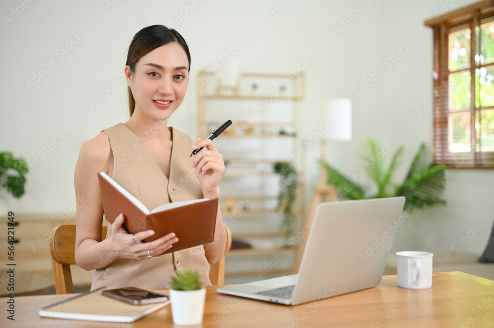 Attractive Asian businesswoman sits at her office desk with notebook and pen in her hand Attractive Asian businesswoman sits at her office desk with notebook and pen in her hand