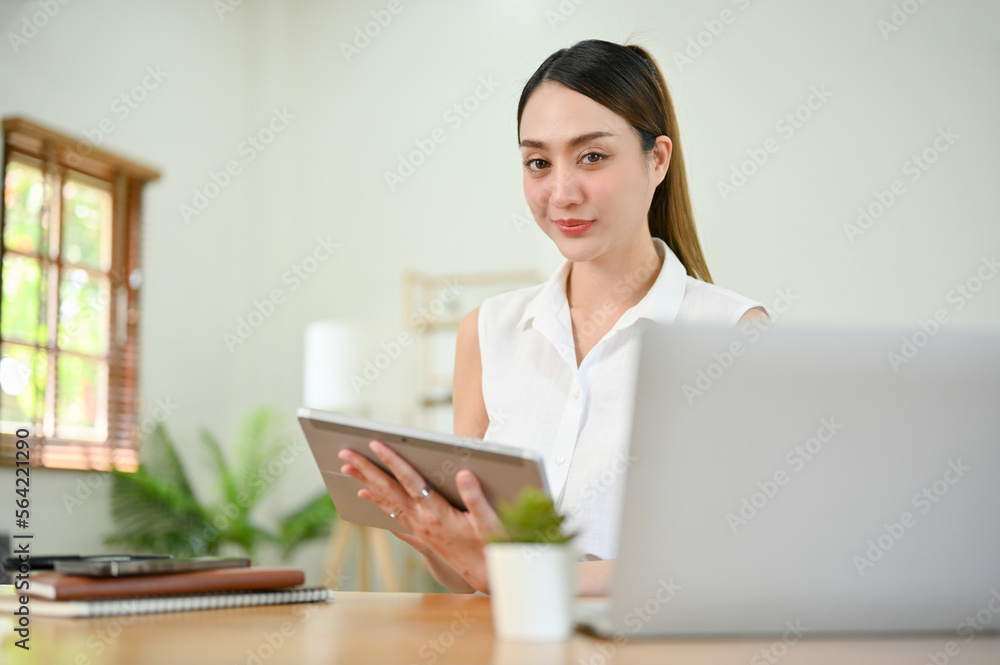 Charming millennial Asian businesswoman sits at her desk with a digital tablet Charming millennial Asian businesswoman sits at her desk with a digital tablet
