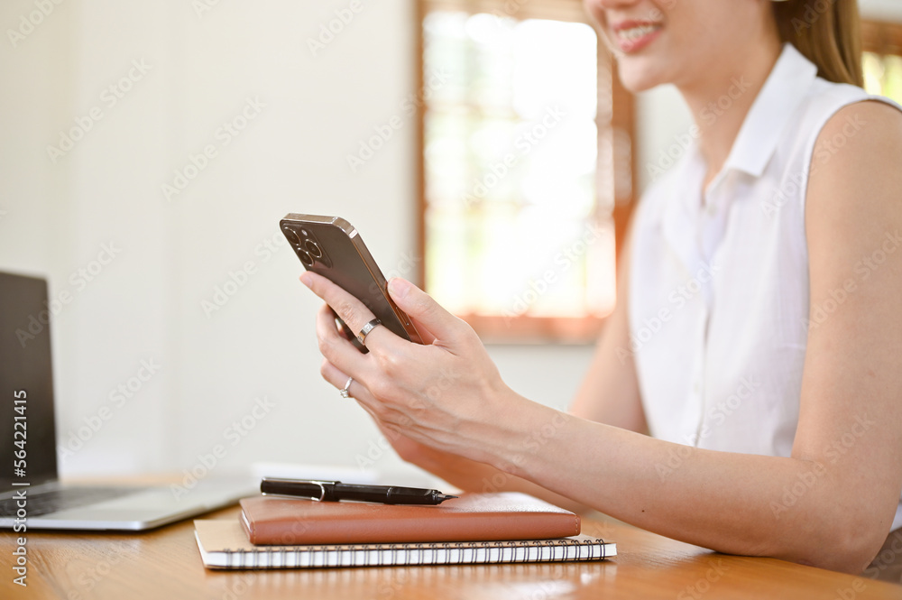 Attractive Asian woman using her phone at her working desk. cropped and side view image Attractive Asian woman using her phone at her working desk. cropped and side view image