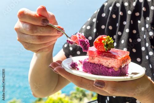 Strawberry cake in a plate in female hands against the backdrop sea. Decorating torts with whole berries. photo