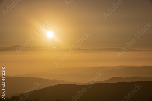 Dramatic sunset on a foggy winter day, shot above the clouds. Mountain range covered with clouds.