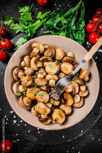 Fried mushrooms in a bowl with greens and tomatoes on a stone board. 