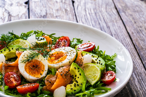 Salmon salad - smoked salmon, hard boiled eggs, avocado and leafy greens on wooden table 