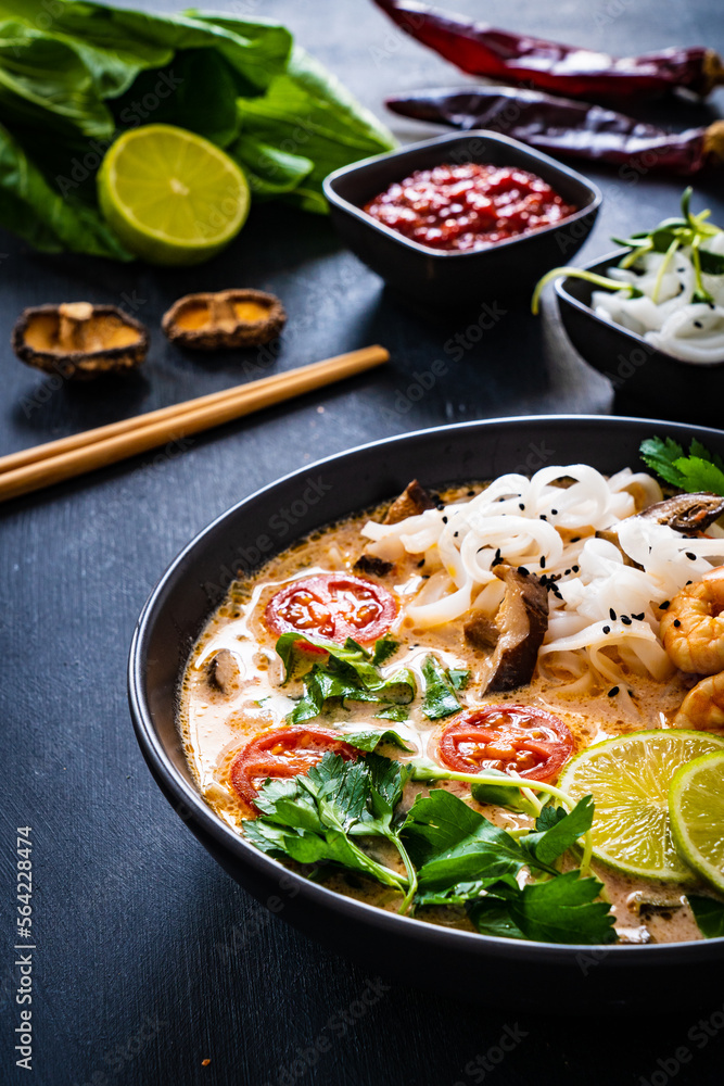 Tom Yum - Thai soup with prawns, shiitake mushrooms and noodles on wooden table
Tom Yum - Thai soup with prawns, shiitake mushrooms and noodles on wooden table