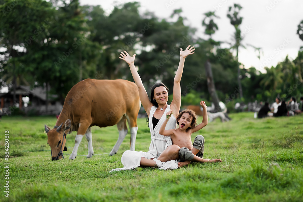 Fototapeta premium Happy mom and son hugging in the meadow, among the cows.