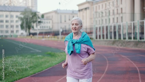 One old lady run marathon stadium. Elderly man jogging distance park. Grandma health care exercises. Senior woman sportsman training. Granny athlete engaged sport. Active lifestyle. People cross race. photo