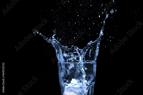 Eiswürfel fällt ins Wasserglas, dunkler Hintergrund