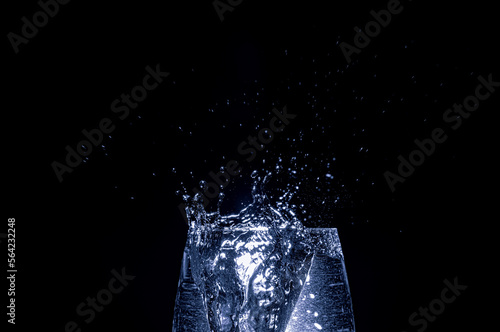 Eiswürfel fällt ins Wasserglas, dunkler Hintergrund