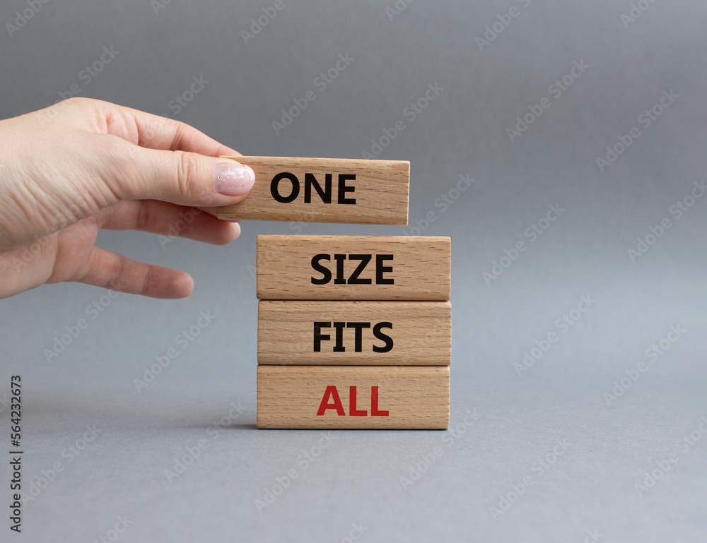 One size fits all symbol. Concept words One size fits all on wooden blocks. Beautiful grey background. Businessman hand. Business and One size fits all concept. Copy space. One size fits all symbol. Concept words One size fits all on wooden blocks. Beautiful grey background. Businessman hand. Business and One size fits all concept. Copy space.