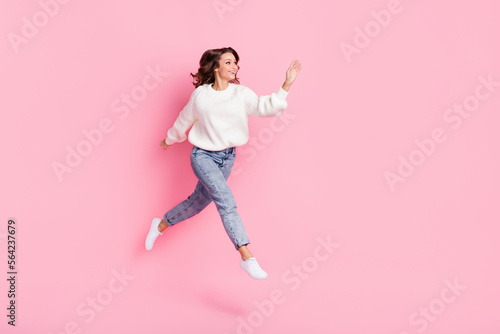 Full length photo of cute friendly woman dressed pullover waving arm empty space jumping high isolated pink color background