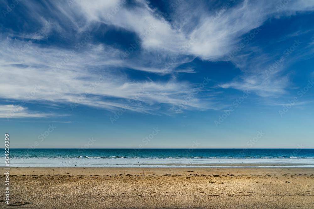 Landscape of an uncrowded beach with white clouds over blue sky in Brittany, France.