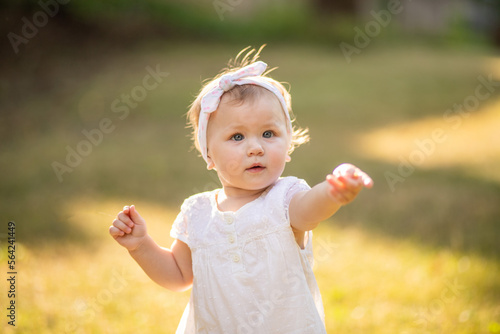 Portrait of a cute cute little girl close-up on a green background of nature. The child points to an object. Pointing gesture typical for children of one year. The piercing gaze of a child. 