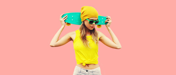 Summer portrait of stylish cool young woman with skateboard wearing colorful clothes on pink background