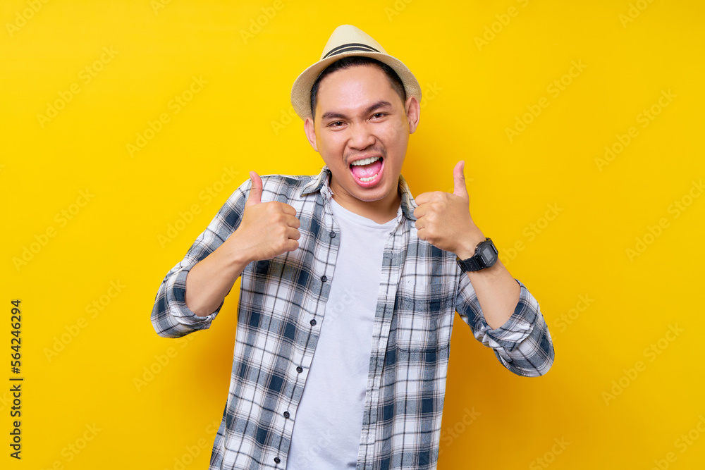 Smiling Young handsome ethnic Asian man 20s wearing casual clothes hat standing confident and showing thumb up like gesture isolated on yellow background. People lifestyle concept