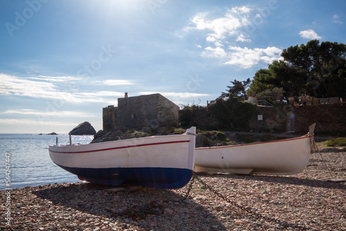 Pareja de barcas estacionadas sobre las piedras de una de las pequeñas playas del pueblo catalán de Cadaqués con el tranquilo y azul mar de fondo.