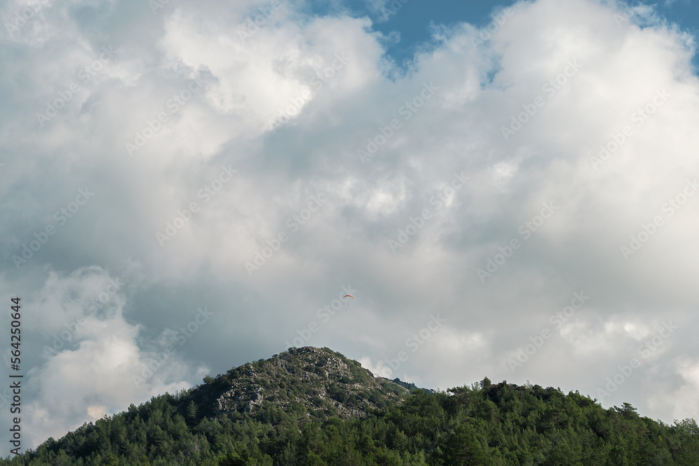 Scenic mountain view with paragliders flying at high altitude and white fluffy clouds, panoramic shot of mountains at noon on the Aegean coast