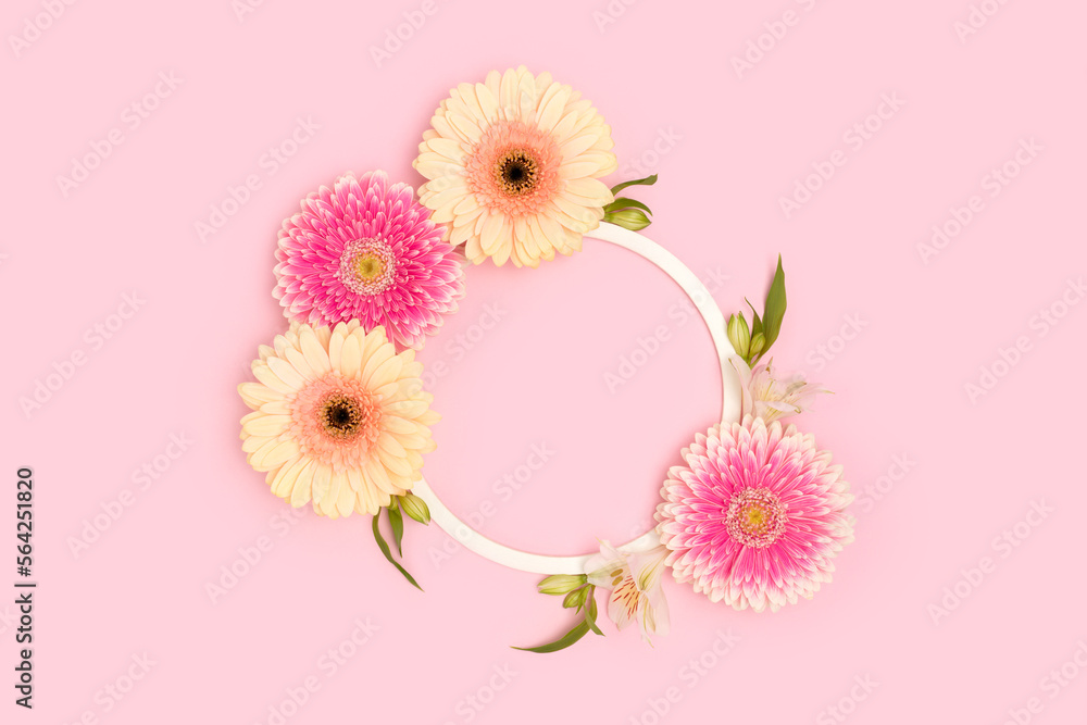 Wreath made of green leaves, alstroemeria and gerbera flowers on a pink background.