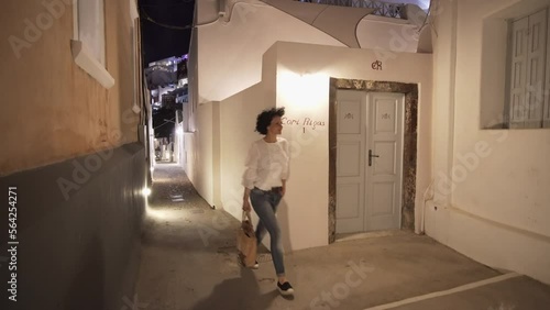 Woman walks on narrow Cori Rigas street in Fira, Santorini at night photo