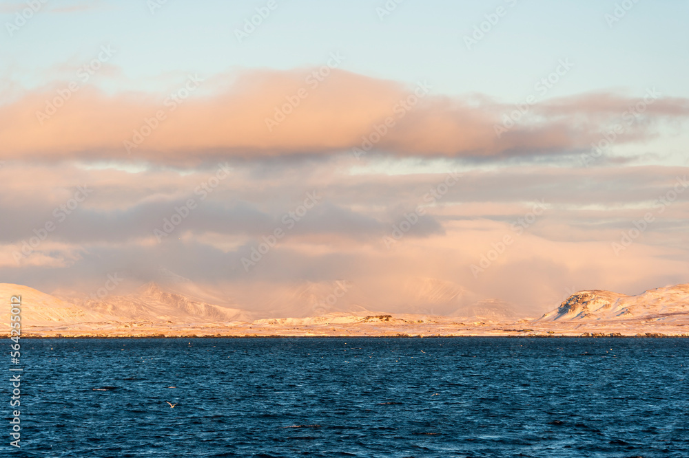 imagen de un paisaje con el mar en la parte inferior, las montañas nevadas al fondo y el cielo azul con nubes 