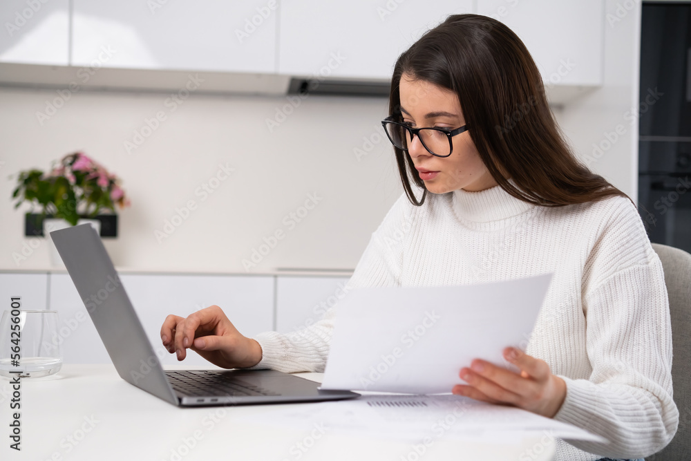 Serious focused businesswoman typing on a laptop holding papers at home and working remotely Serious focused businesswoman typing on a laptop holding papers at home and working remotely