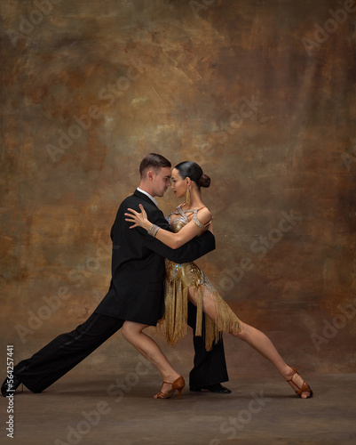 Passionate couple dancing. Man and woman, professional dancers performing ballroom dance over dark vintage background. Theatrical performance. Concept of hobby, lifestyle, action, motion, attraction