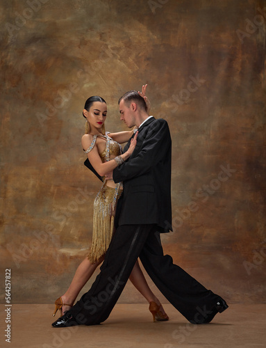 Man and woman, professional tango dancers in stylish, beautiful stage costumes performing over dark vintage background. Couple dance style. Concept of hobby, lifestyle, action, motion.