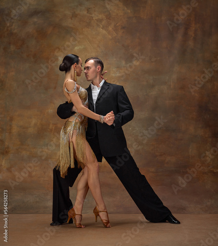 Deep, impressive look. Man and woman, professional tango dancers in stylish, beautiful stage costumes performing over dark vintage background. Concept of hobby, lifestyle, action, motion.