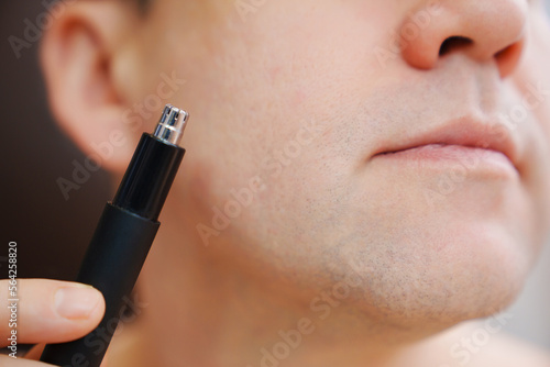 close-up. a man cwith trimmers for cutting hair in the nose and ears. the concept of personal hygiene and removal of excess hair. photo