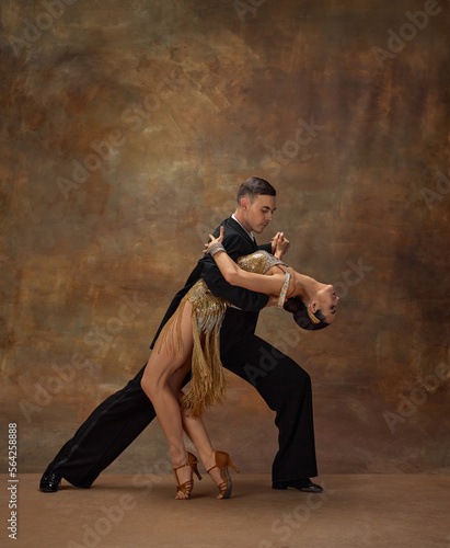 Passion, emotions. Man and woman, professional tango dancers in stylish, beautiful stage costumes performing over dark vintage background. Concept of hobby, lifestyle, action, motion, dance aesthetics