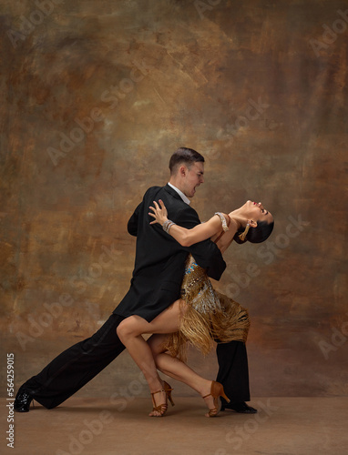 Man and woman, professional tango dancers in stylish, beautiful stage costumes performing over dark vintage background. Passionate performance. Concept of hobby, lifestyle, motion, dance aesthetics
