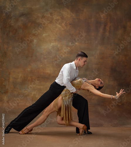 Man and woman, professional tango dancers in stylish, beautiful stage costumes performing over dark vintage background. Art of movements. Concept of hobby, lifestyle, action, motion, dance aesthetics