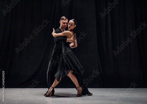 Style, passion, romance. Man and woman, professional tango dancers performing in black stage costumes over black background. Concept of hobby, lifestyle, action, motion, art, dance aesthetics