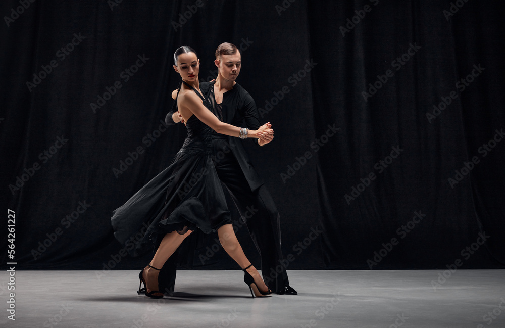 Impressive passionate performance. Man and woman, professional tango dancers performing in black stage costumes on black background. Concept of hobby, lifestyle, action, motion, art, dance aesthetics