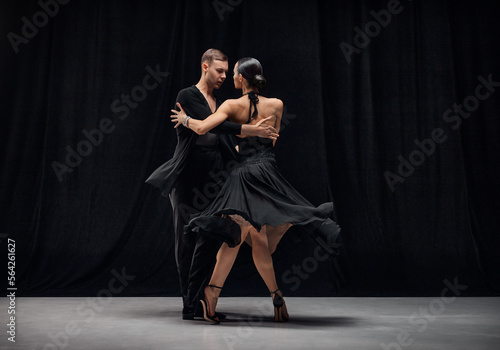 Romantic couple dance. Man and woman, professional tango dancers performing in black stage costumes over black background. Concept of hobby, lifestyle, action, motion, art, dance aesthetics
