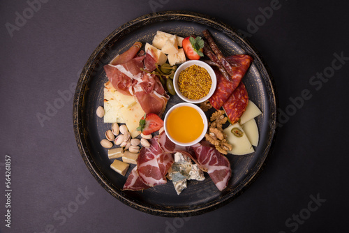 delicious meat assortment, cumin sauce, pistachios, strawberries, cheese, nuts in a black plate on a black background
