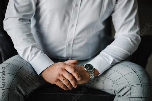 Male hands with wedding ring and watch. The man is sitting on the couch. Hands of the groom with an engagement ring. Close-up folded man's hands. Stylish man concept.