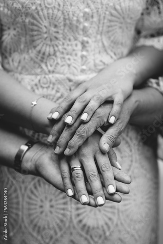 Different generations: daughter, mother, grandmother, man and grandfather. Focus on hands. Unrecognizable grandmother and her granddaughter holding hands. Close up. Black and white photo.