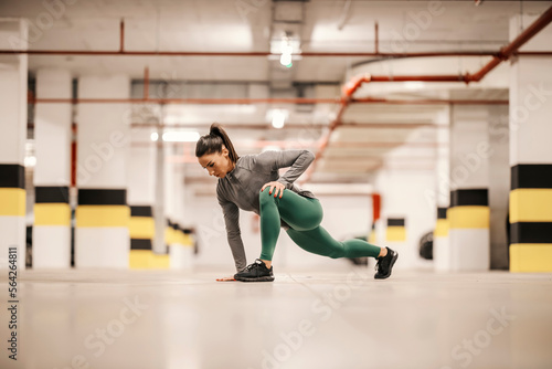 A fit sportswoman is stretching her leg in underground garage.