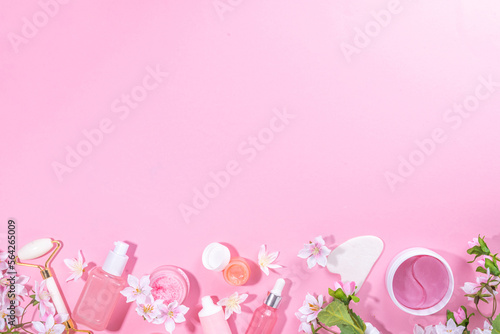 Spring skin care cosmetics flat lay. Beauty facial care cosmetics: serum, cream, mask on pink sunny background with spring blossom flowers, top view copy space