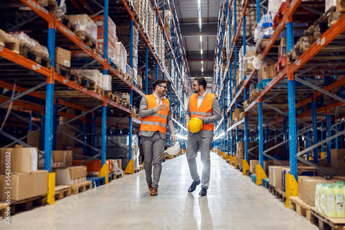 Foto Two associates walks in warehouse full of goods and talks about commodity reserves