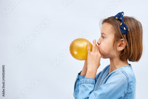 Fotografi Pretty little girl in casual denim dress blowing, inflate yellow balloon on whit