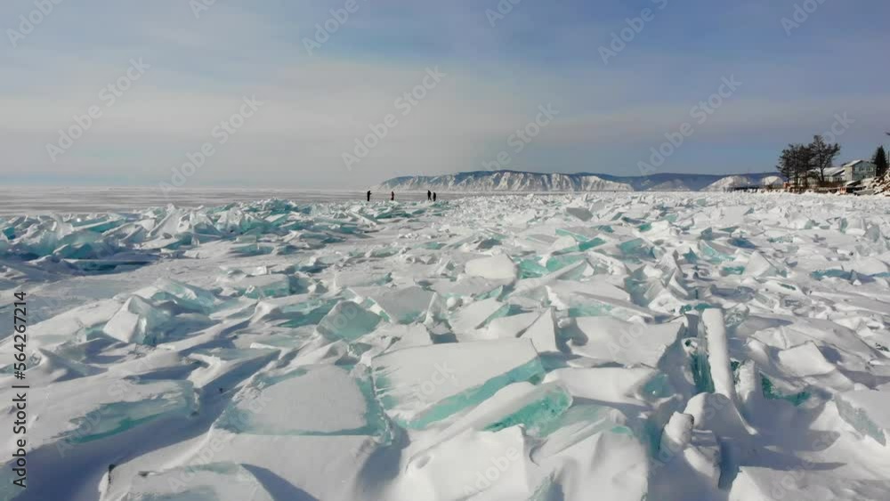 Hummocks, blocks of transparent ice, large ice floes near the shore of frozen Lake Baikal. Listvyanka village. Tourists walk on the ice of the lake on a sunny winter day. Hummocks, blocks of transparent ice, large ice floes near the shore of frozen Lake Baikal. Listvyanka village. Tourists walk on the ice of the lake on a sunny winter day.