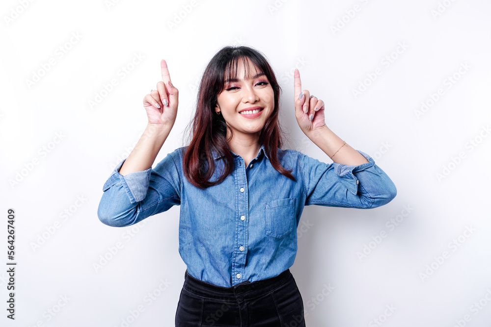 Excited Asian woman wearing blue shirt pointing at the copy space on top of her, isolated by white background
