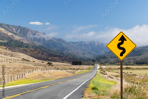 Asphalt road, sign and country landscape with sunny sky