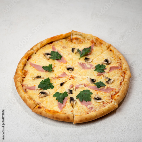 Pizza with mushrooms, ham and cheese on white background. Pizza is cut into portioned pieces, decorated with parsley. Serving the dish. View from above. 