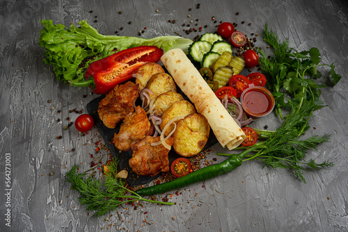 Turkey meat on the grill with fried potatoes, cucumbers, cherry tomatoes and ketchup on a gray background, pita bread, greens, dill