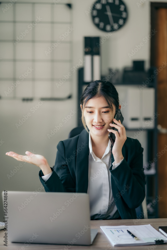 business woman talking mobile phone and working on laptop and papers on table in her office. business woman talking mobile phone and working on laptop and papers on table in her office.