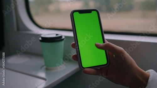 Close-up of a woman's hand with a mobile phone with a green screen in a train carriage. Place for advertising