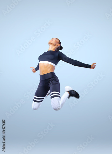 Attractive excited fitness girl, ballerina dancer in sportwear jumping of joy isolated over gray background.